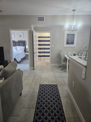 Une chambre d’hôtel comprenant un lit, un coin salon avec un canapé, une salle de bain avec douche et un couloir menant à une autre pièce.
