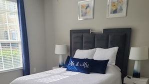 A bedroom with a large bed, two nightstands, a ceiling fan, and artwork on the walls. - Ground floor pool view retreat with free parking.  (Clearwater)
