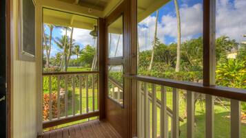 A wooden porch with a view of a tropical garden and palm trees.