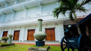 A building with a white facade, large wooden doors, and a traditional cannon labeled "ORIENT" in front. - Euro Star Hotel (Seeduwa - Katunayake)
