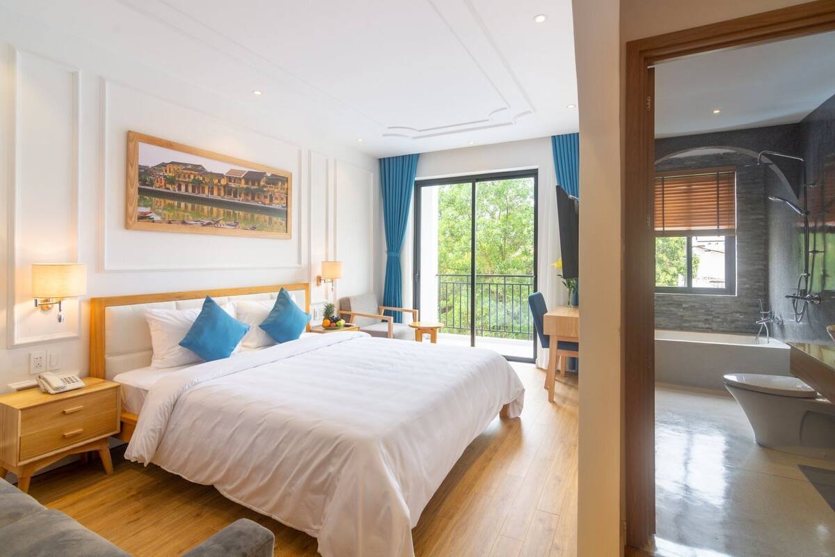 A hotel room with a large bed, a desk, a chair, a balcony, and a bathroom.