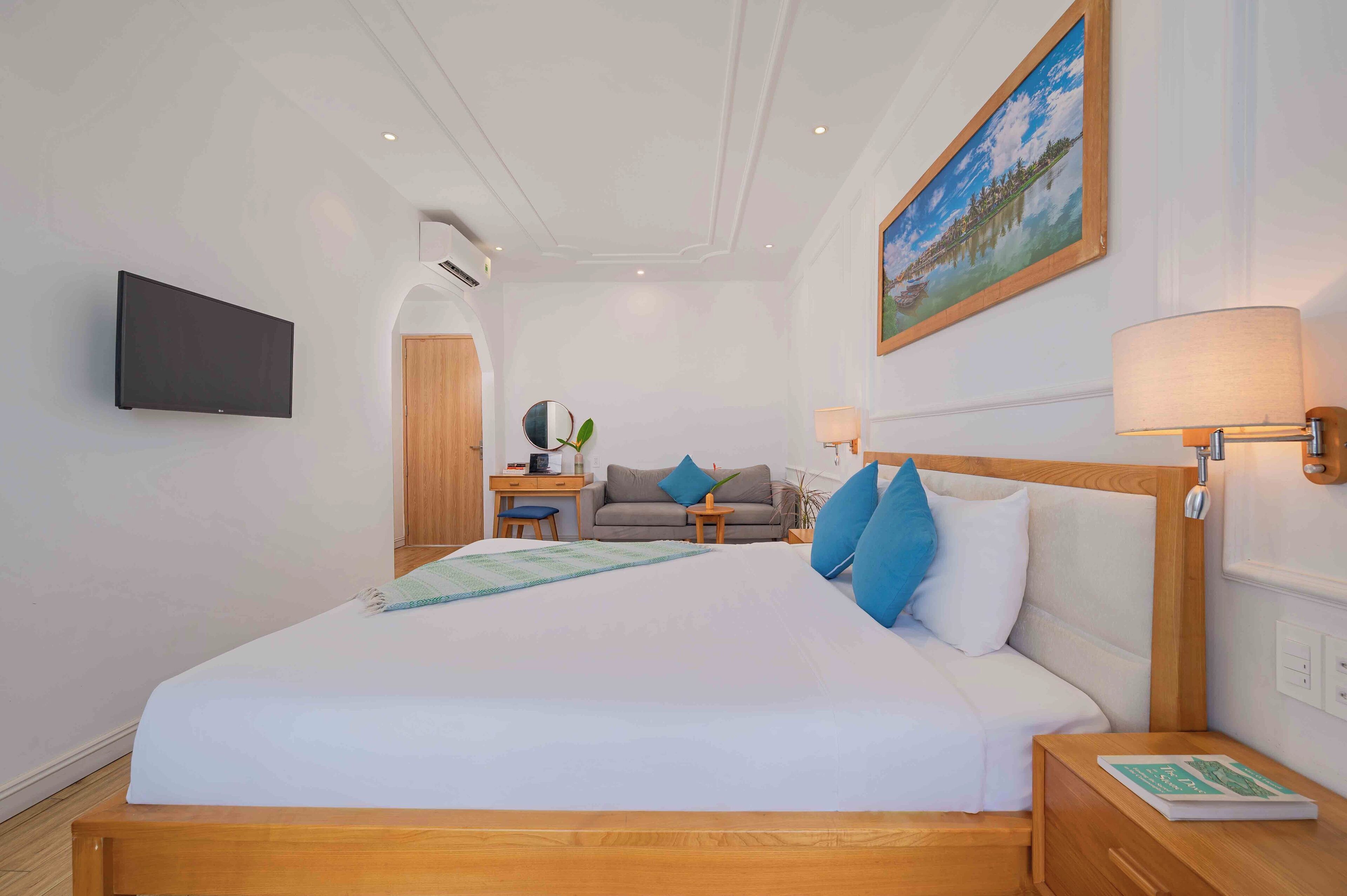 Una habitación de hotel con una cama grande, un televisor montado en la pared, un cuadro sobre la cama y una lámpara en la mesita de noche.