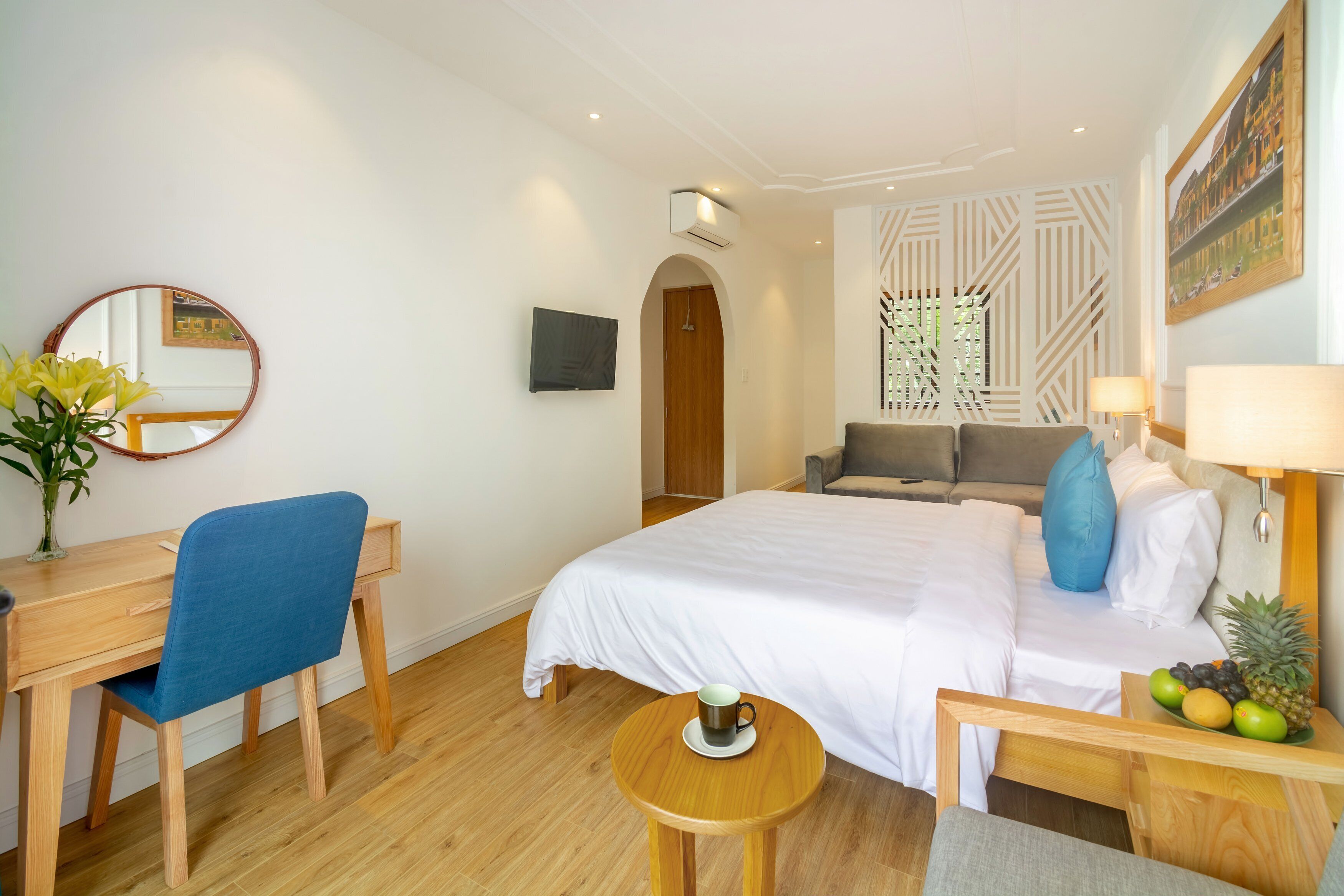 A hotel room with a bed, a desk, a chair, a round table, a TV, and a fruit basket.
