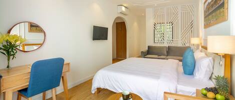 A hotel room with a bed, a desk, a chair, a round table, a TV, and a fruit basket.