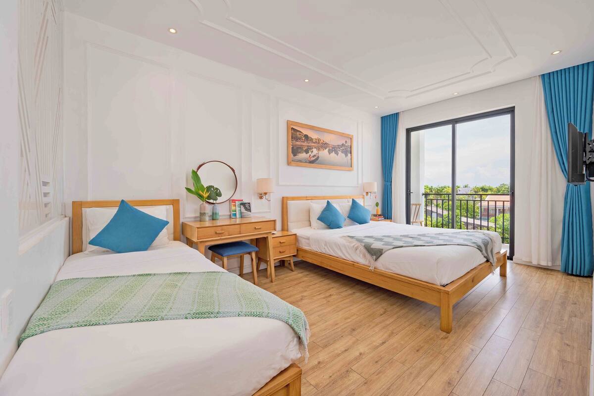 A hotel room with two beds, a desk, a chair, a TV, and a large window with a view.
