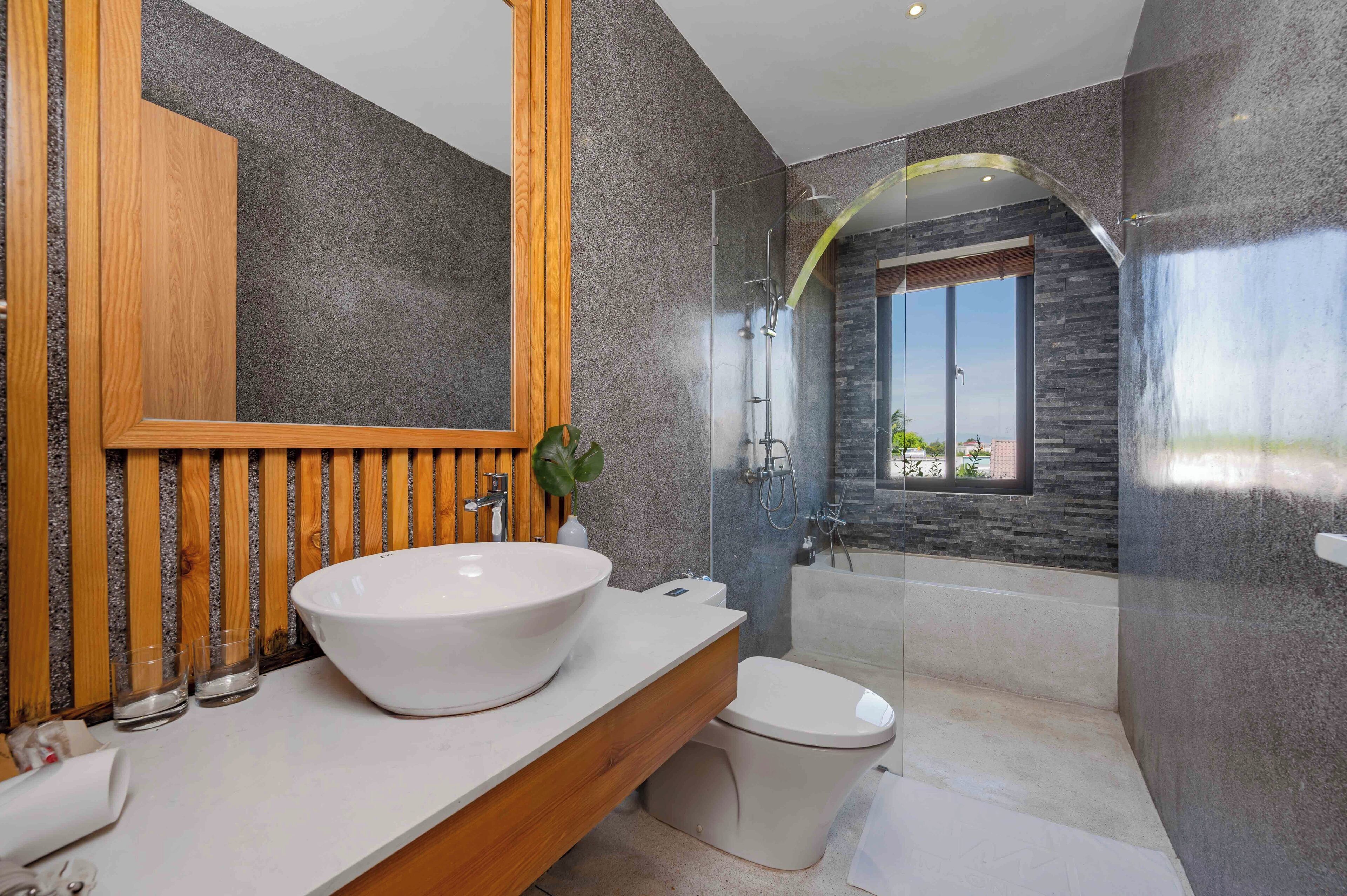 A modern bathroom with a large white sink, a wooden vanity, a glass-enclosed shower, and a view of the outdoors.
