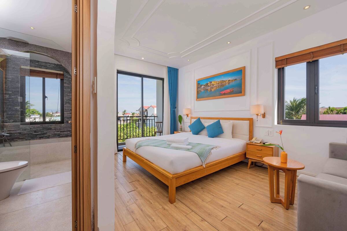 A modern hotel room with a large bed, a balcony, and a painting on the wall.
