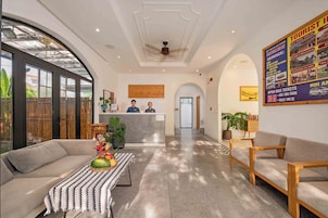 Un vestíbulo de hotel con mostrador de recepción, sofás, una mesa baja con fruta y un cartel que anuncia tours turísticos.