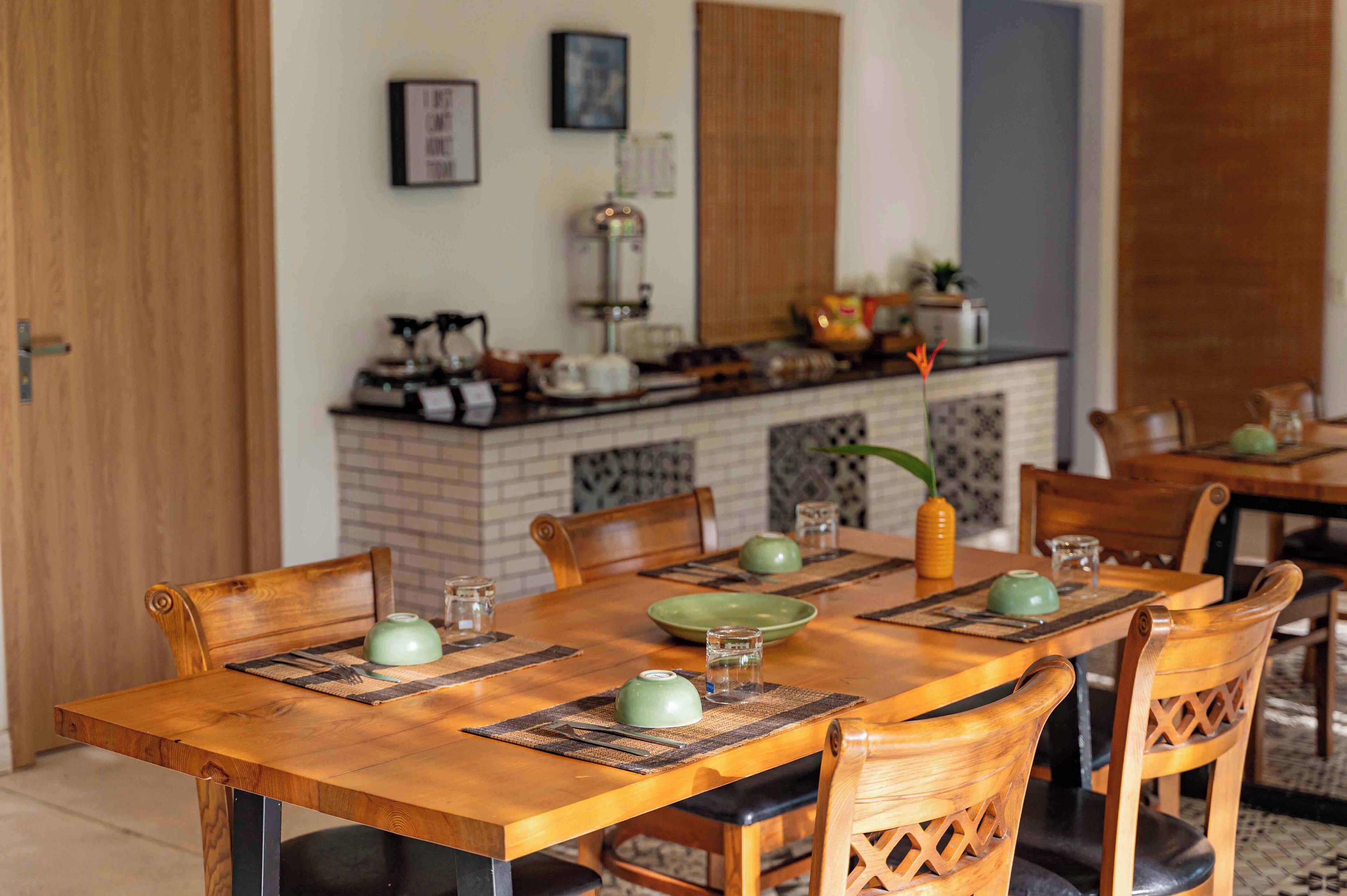 A wooden dining table with chairs, a kitchen area with a coffee machine, and a brick backsplash.