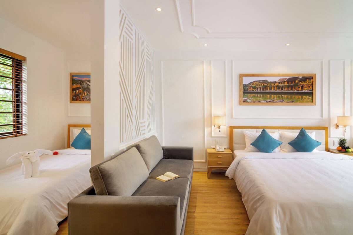 A hotel room with two beds, a sofa, a decorative wall panel, and artwork on the walls.