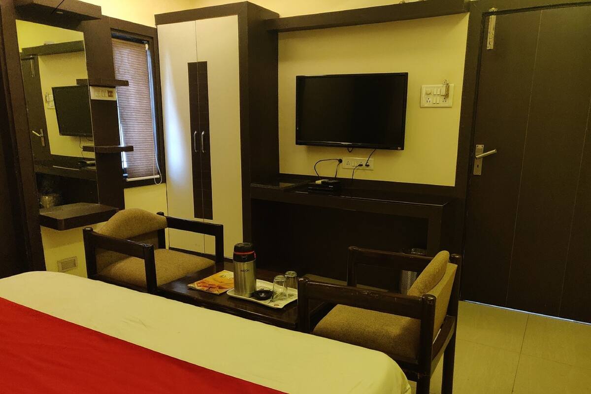A hotel room with a bed, a desk with a chair, a television, and a mirror.