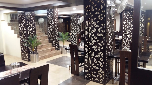 A modern hotel lobby with a staircase, decorative screens, and a dining area. - Hotel Rahul (Jabalpur)