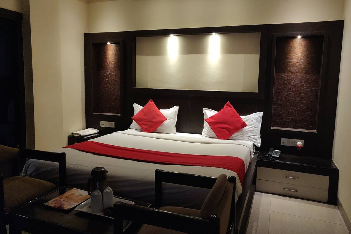 A hotel room with a large bed, a desk with a chair, a nightstand, and a wall-mounted TV.