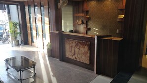 A reception area with a marble counter, wooden paneling, and a glass table. - Hotel Rahul (Jabalpur)
