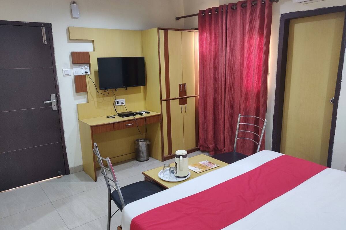 A hotel room with a bed, a desk with a TV, a chair, a trash bin, and a wardrobe.