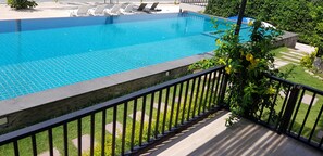 A clear blue swimming pool with a stone border, surrounded by a wooden deck and a metal railing. - Samutra Residences (Ko Pha-ngan)