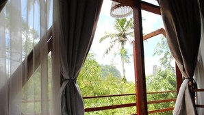 Una habitación con cama, cortinas de gasa y vistas al verde exterior.