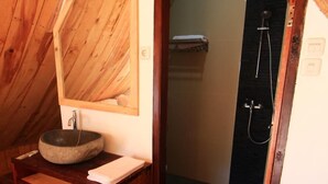 Un baño con tocador de madera, lavamanos de piedra, espejo y zona de ducha.