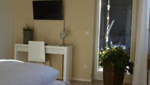Un dormitorio con cama, escritorio, silla, televisor y una planta en maceta.