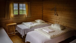 Una cabaña con dos camas individuales, una mesita y una ventana con cortinas.