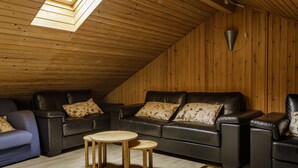 Una sala de estar estilo loft acogedora, con techo inclinado, paredes de madera y un sofá de cuero negro.