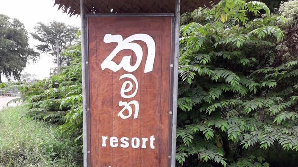 A wooden sign for a resort with a thatched roof, surrounded by lush greenery. - Kamatha Resort (Polonnaruwa)