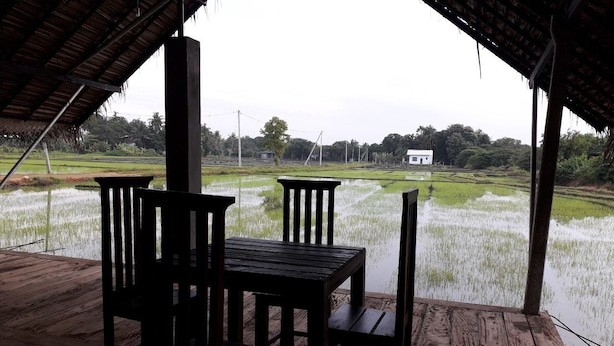A wooden table and chairs under a thatched roof, overlooking a rice paddy field. - Kamatha Resort (Polonnaruwa)
