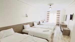 A hotel room with four beds arranged in a row, a wooden headboard, a small wooden side table, and a mirror on the wall. -  Van Toprak Hotel (Van)