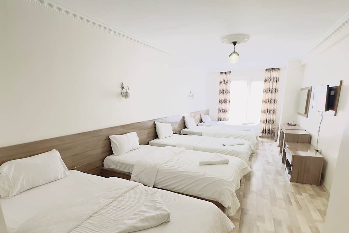 Habitación de hotel con cuatro camas dispuestas en fila, cabecera de madera, mesita de noche de madera y un espejo en la pared.