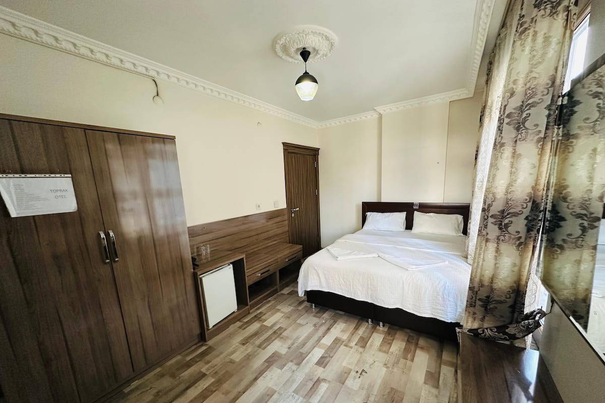 Una habitación de hotel con un armario de madera, una cama con ropa blanca, un escritorio y una cortina estampada.