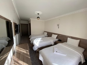 A hotel room with three beds, a wooden floor, a ceiling light, and a wall-mounted TV.