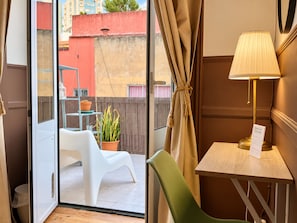 Quarto com porta de vidro deslizante que dá para área externa com uma cadeira branca, uma cadeira verde e uma mesa com abajur.