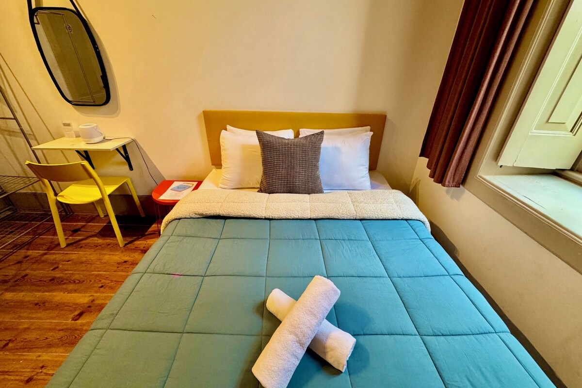 A hotel room with a bed, a small table, a chair, and a mirror.