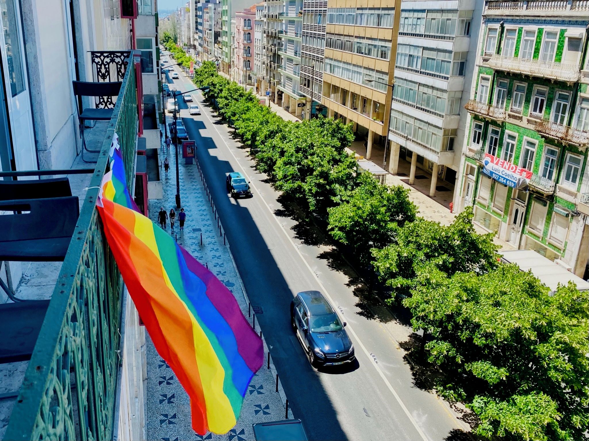 A street view with a rainbow flag, buildings, and parked cars.