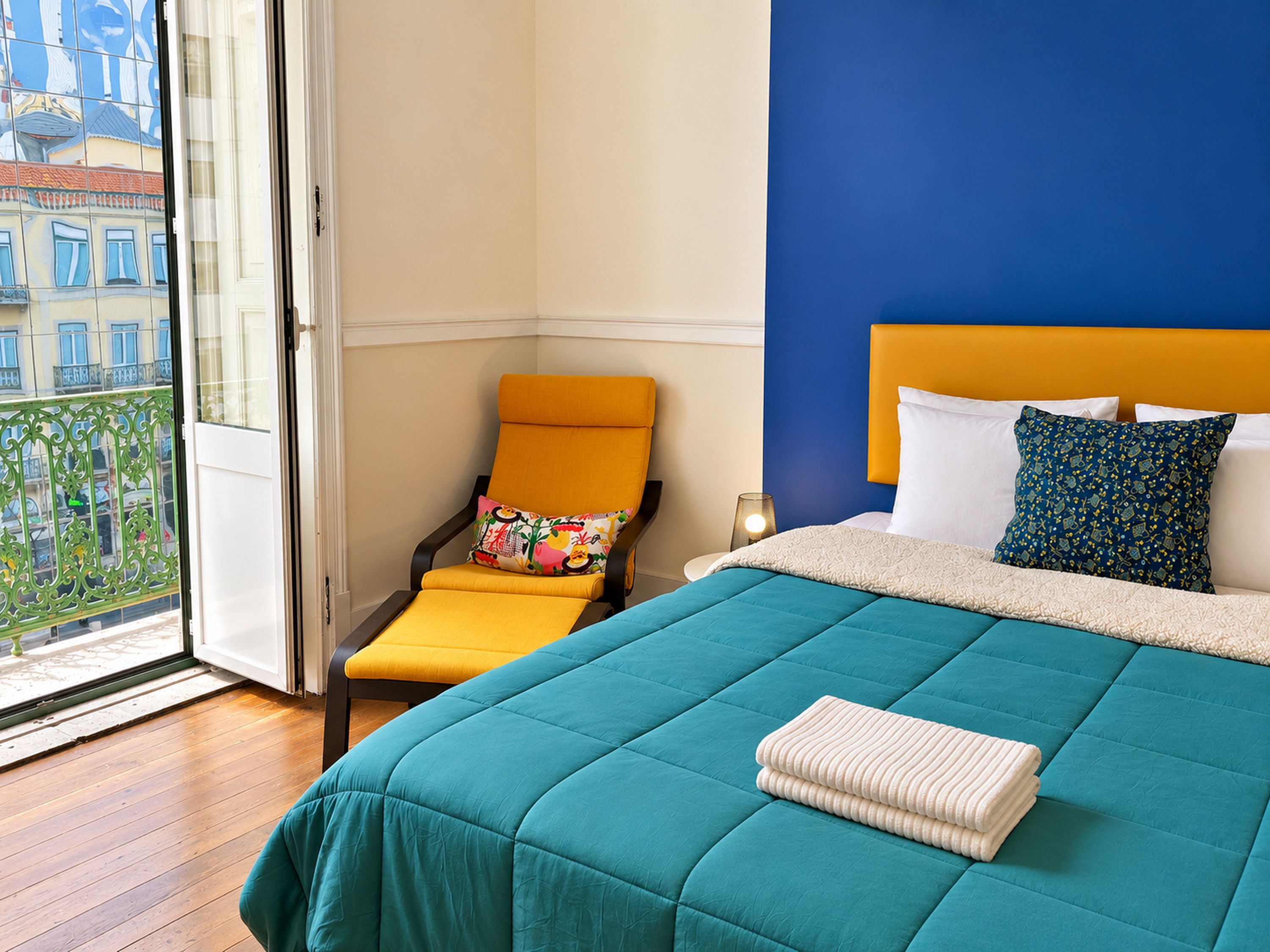 Une chambre d’hôtel avec un lit, une chaise, une table de chevet et une vue sur la ville, visible à travers une porte vitrée.