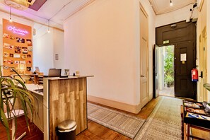 A reception desk with a laptop, a bulletin board with photos, and a plant. - Ambiente Hostel (Lisbon)