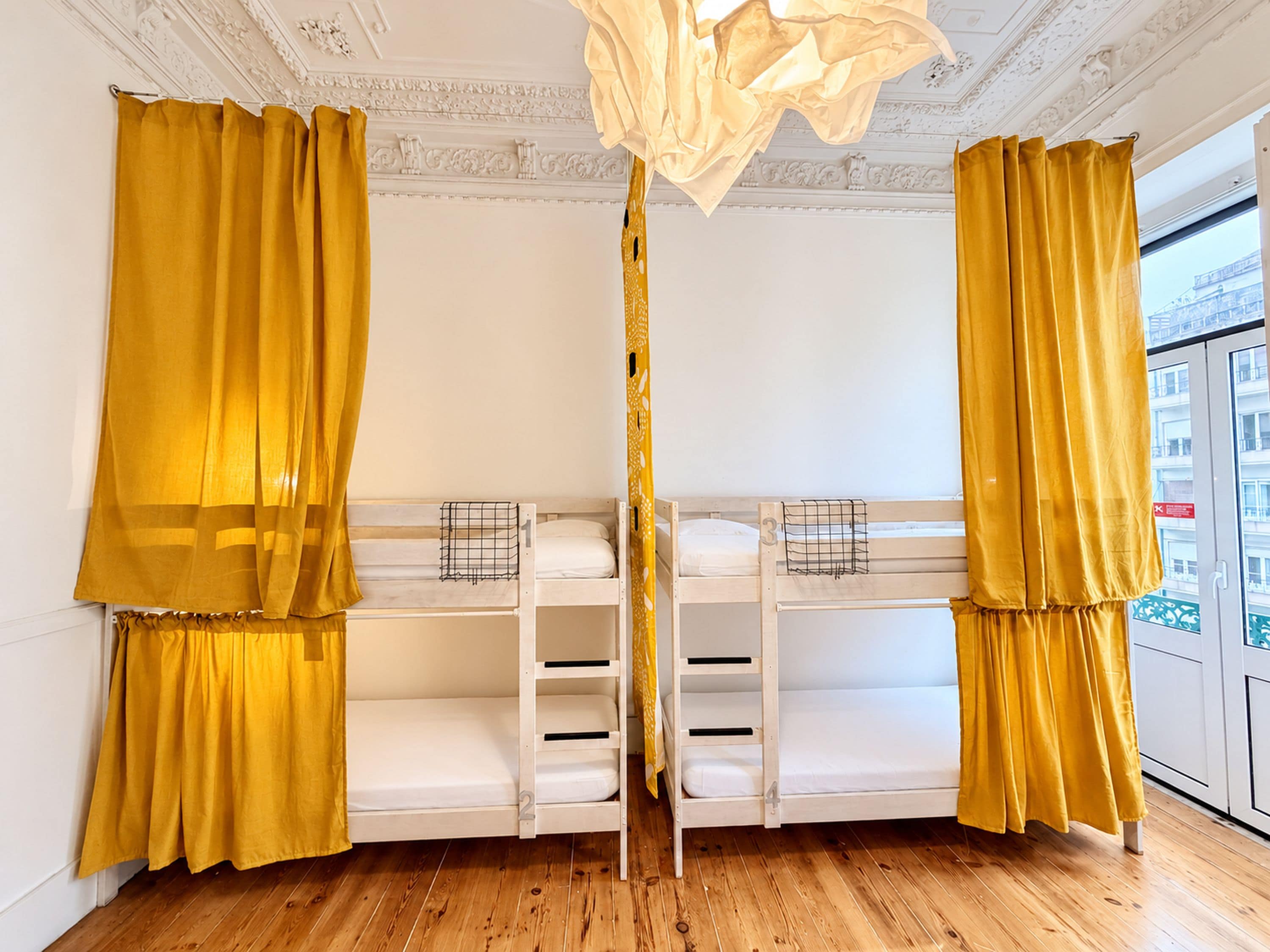 A room with two bunk beds, a window with curtains, and a chandelier.