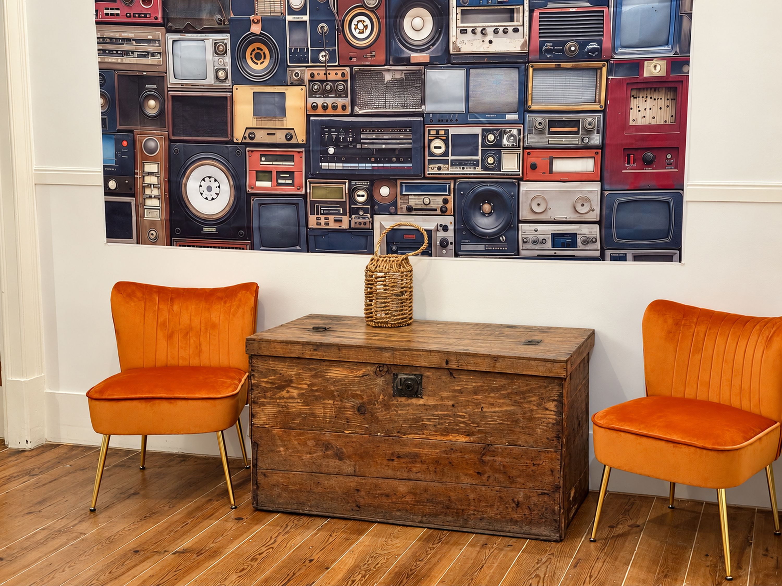 Una habitación con dos sillas naranjas, un cofre de madera y una pared decorada con equipo de audio antiguo.