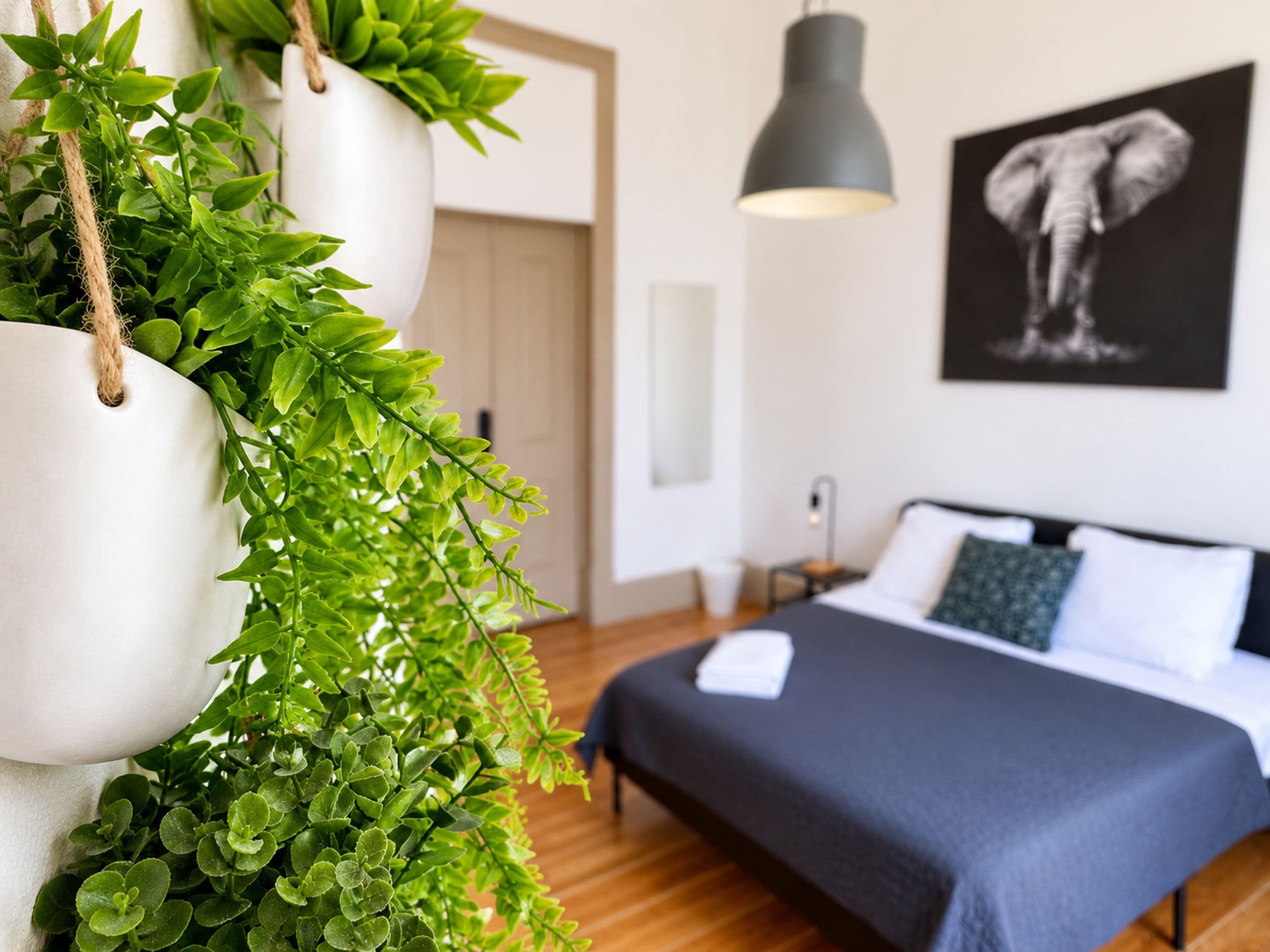 Une chambre à coucher avec un lit, une plante suspendue, un luminaire suspendu et un tableau accroché au mur.