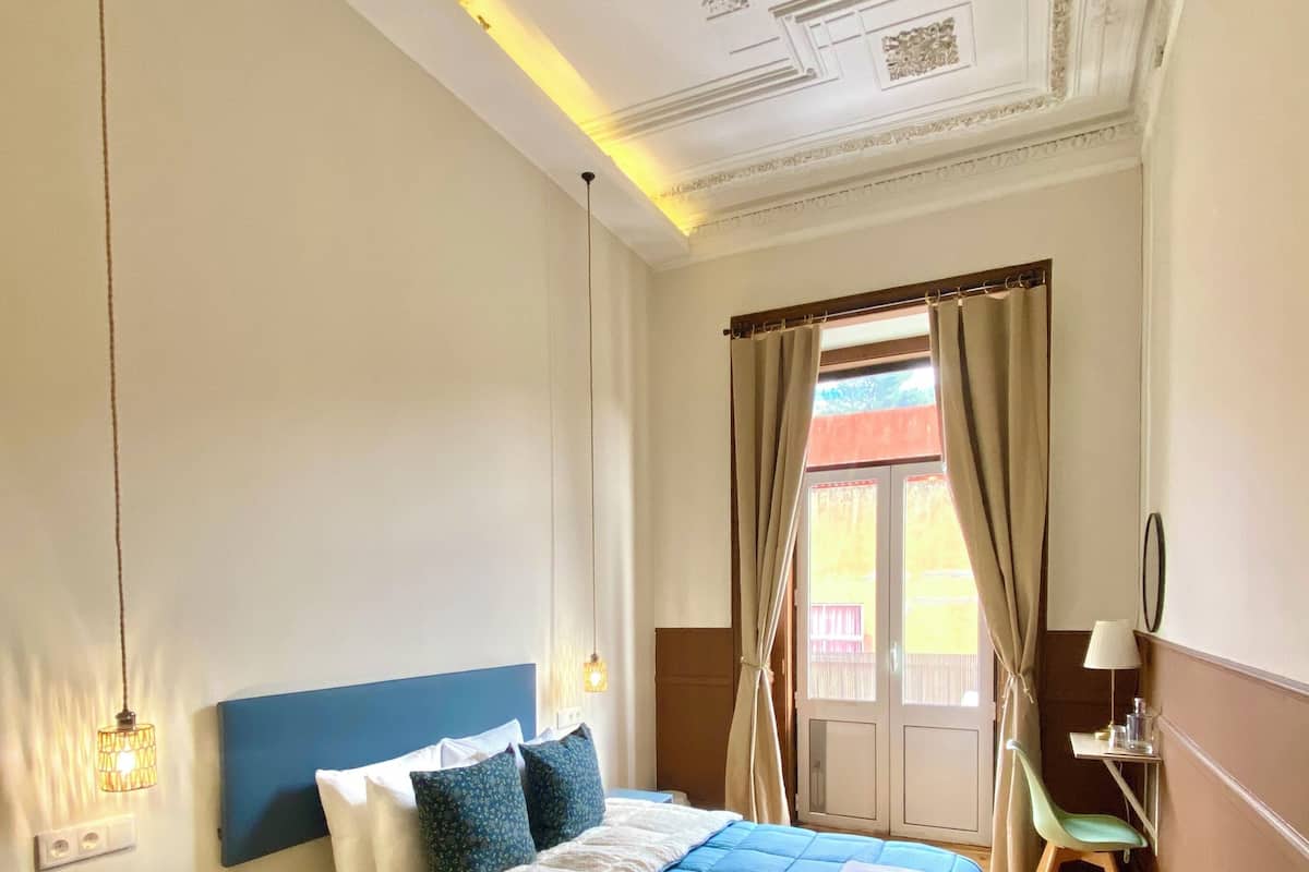 Une chambre à coucher avec un lit, une table de chevet, une lampe et une vue sur l’extérieur.