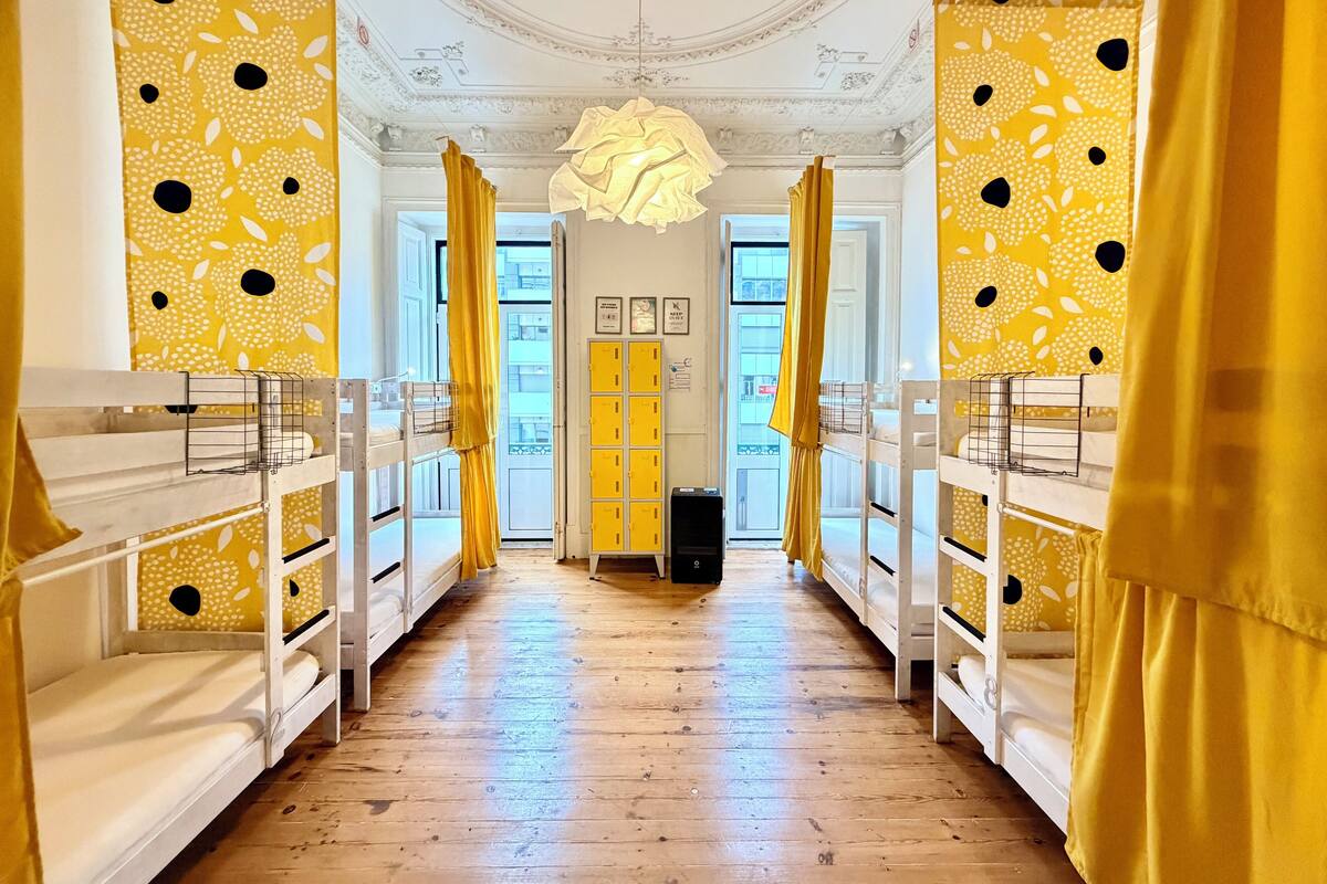 Un couloir avec des lits superposés, des rideaux jaunes et un lustre.