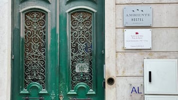 Une porte verte à deux battants ornée de motifs métalliques complexes, une enseigne indiquant « Ambiente Hostel » sur le mur, et un petit panneau indiquant « Rosa de Saron ».