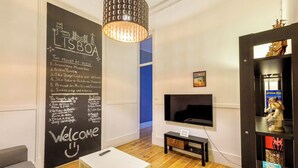 A modern living room with a blackboard listing top places to visit in Lisbon, a TV, and a wooden floor. - Ambiente Hostel (Lisbon)
