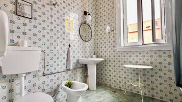 Une salle de bain comprenant des toilettes, un bidet, un lavabo et une petite table.
