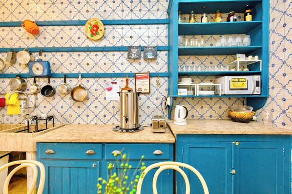 A kitchen with blue cabinets, a tiled backsplash, and various kitchen appliances. - Ambiente Hostel (Lisbon)