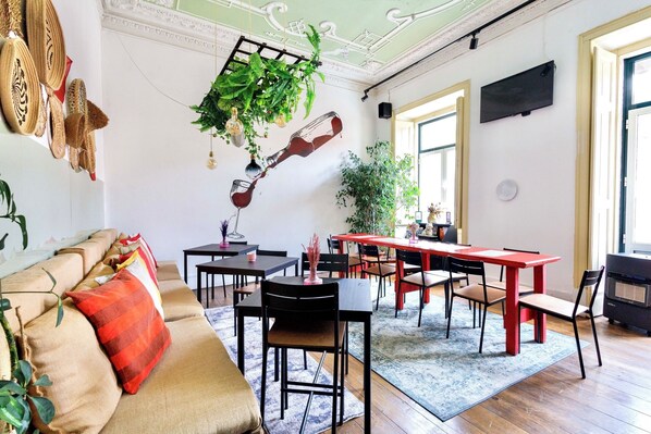 A modern living room with a sofa, dining table, chairs, and a hanging plant. - Ambiente Hostel (Lisbon)
