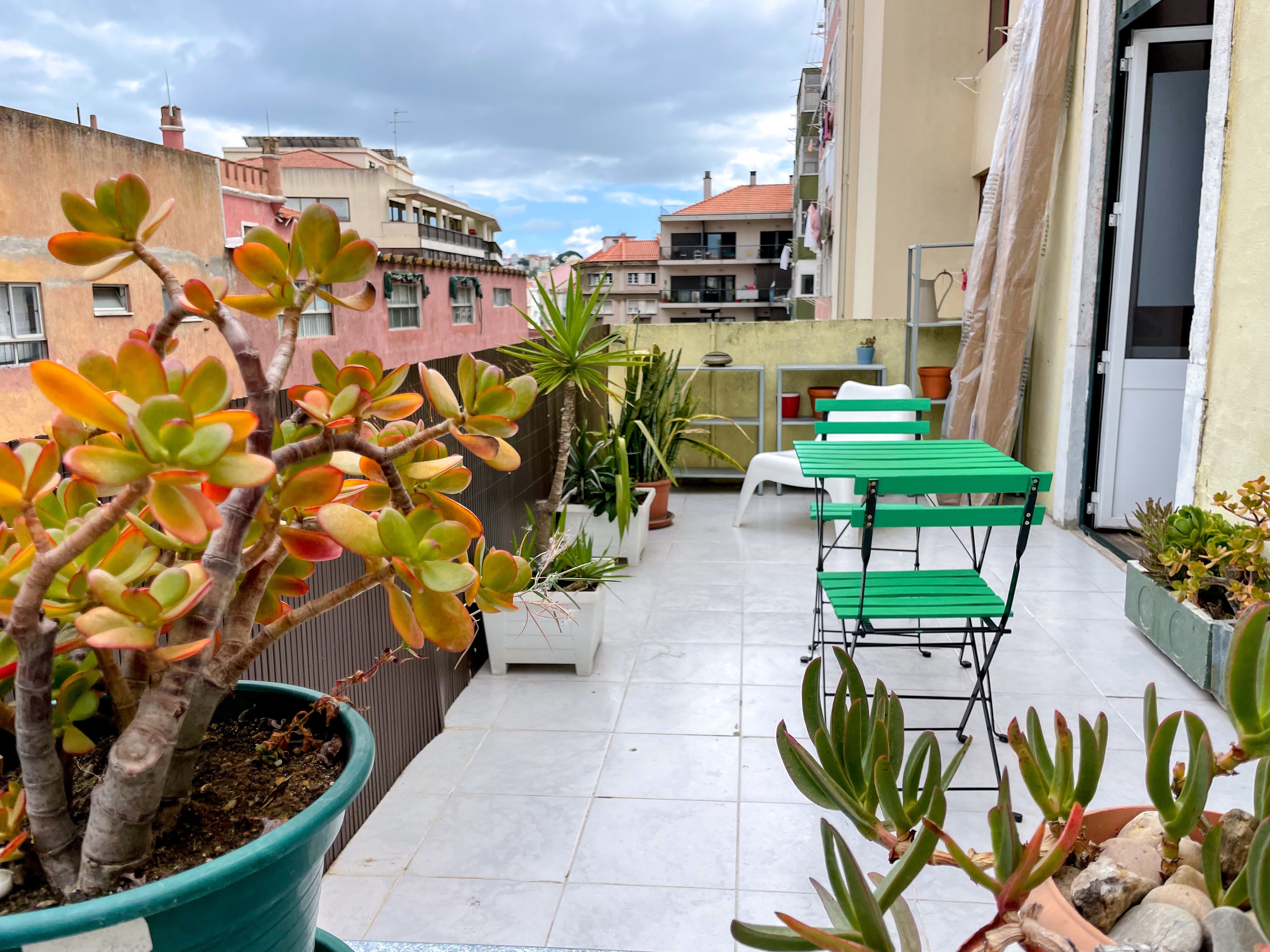 A rooftop terrace with potted plants, a green metal table, and chairs.