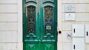 A green door with ornate metalwork, a sign for 'AMBIENTE HOSTEL', and a utility box with a black handle. - Ambiente Hostel (Lisbon)
