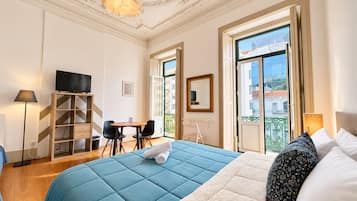 Een hotelkamer met een bed, een bureau, een stoel, een televisie en een balkon met uitzicht.