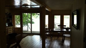A spacious room with wooden floors, a dining table with chairs, a large window, and a ceiling fan. - Vermont lake house,Vermont get away, come and relax (Elmore)